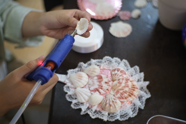 Huyen sticks glue to a piece of seashell to adorn a mirror. Photo: Ngoc Phuong / Tuoi Tre News